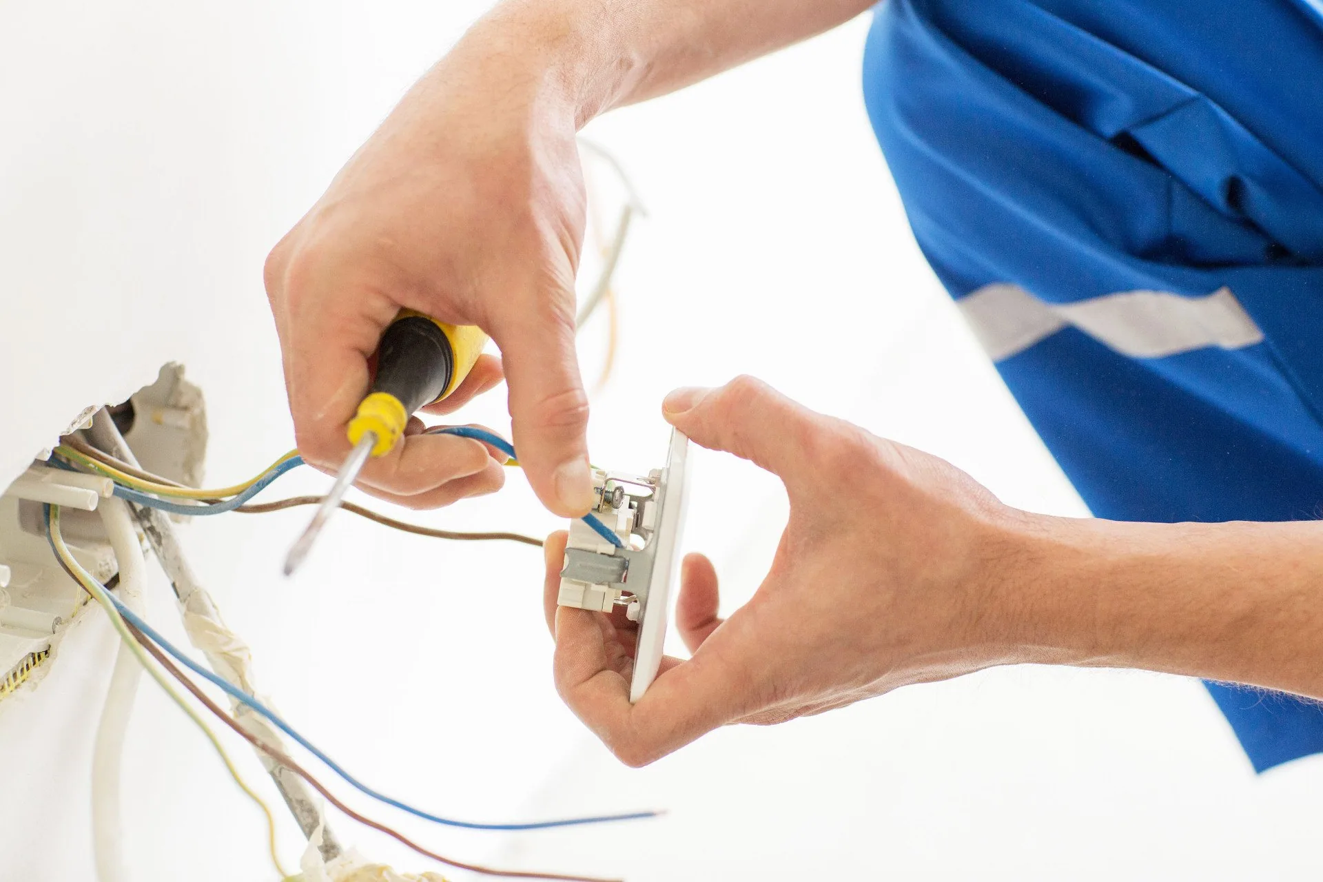 Blue uniform electrician wiring wall outlet screwdriver