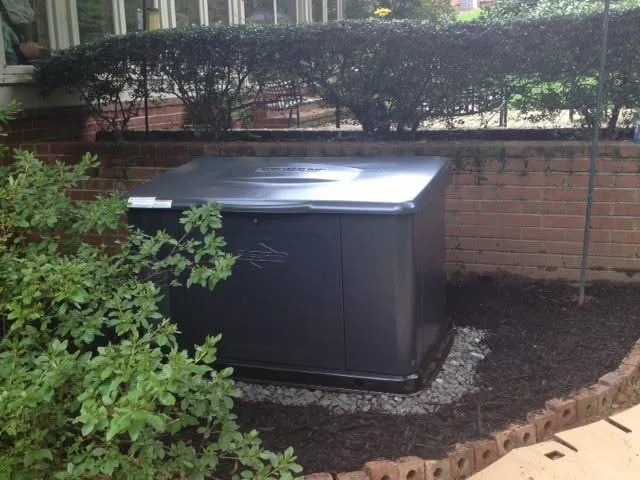 Gray standby generator brick wall mulch bed